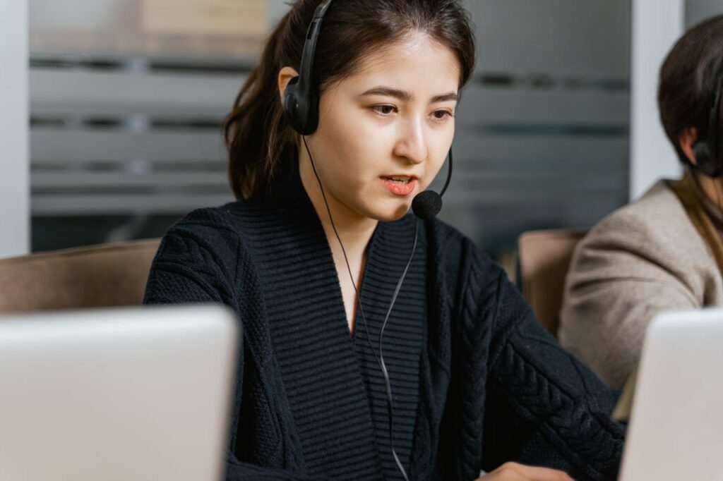 pexels-photo-7709128 Asian woman in a call center focused on customer support tasks using a laptop.